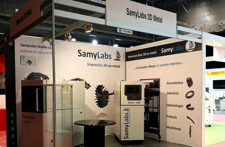 Stand de SamyLabs en ADDIT3D 2018, con la máquina y un expositor de piezas metálicas impresas