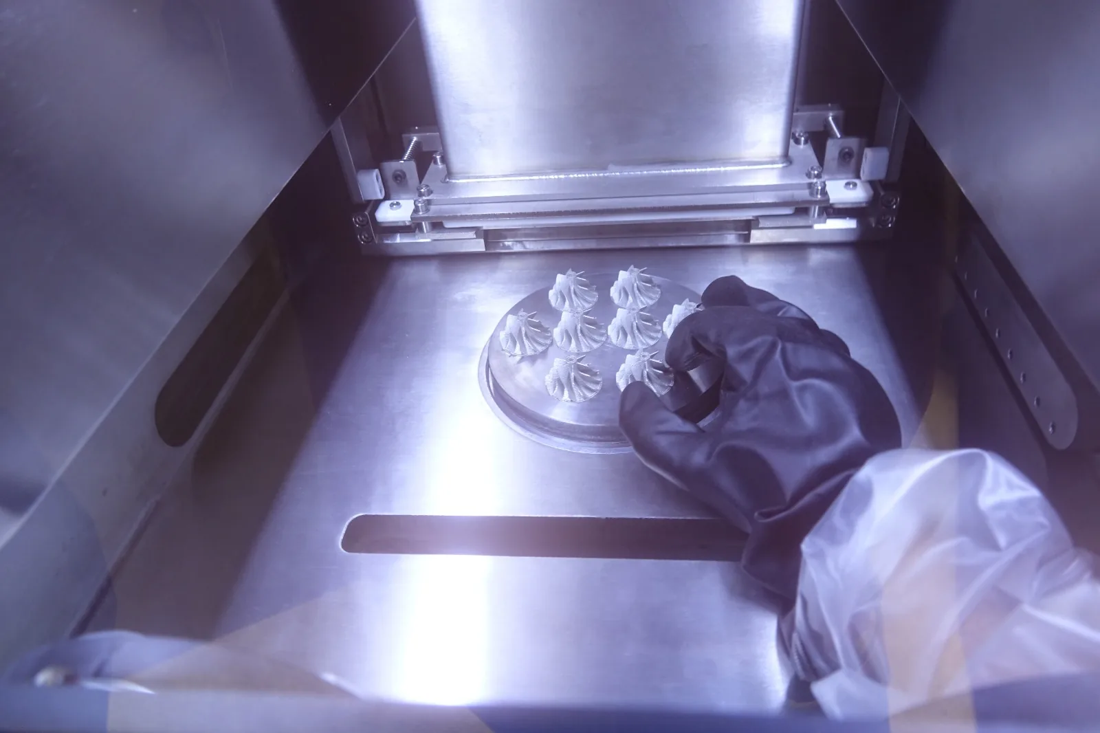 Rodetes de turbina impresos en metal sobre la plataforma, manipulados con los guantes integrados en la cámara