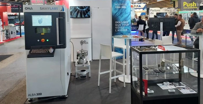 Stand de ONA Electroerosión y SamyLabs en Global Industrie, con la ALBA 300 y una vitrina de piezas impresas